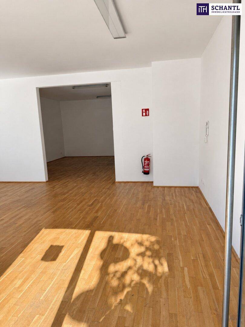 Offener Geschäftsraum mit Holzboden und einem Feuerlöscher an der Wand, bietet flexible Nutzung.