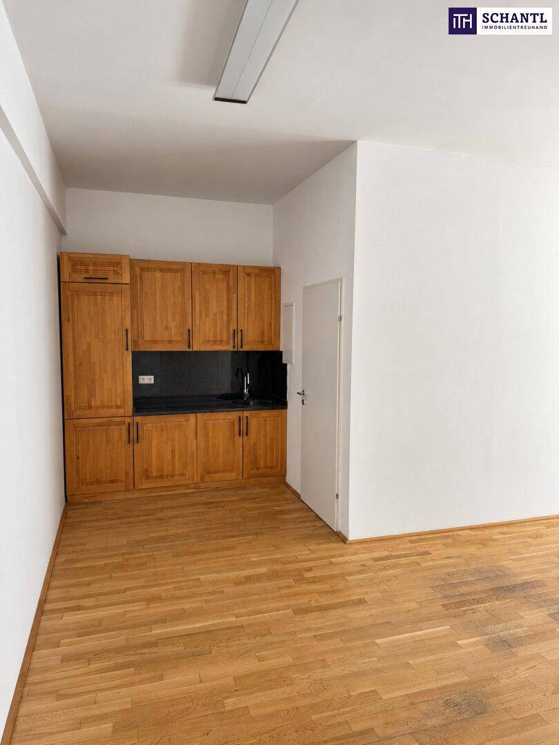 Kleine Küchenzeile mit Holzschränken und schwarzer Arbeitsplatte in einem hellen Raum.