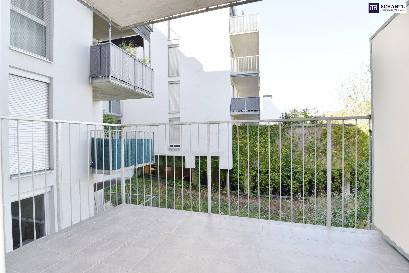 Balkon mit Metallgeländer und Blick auf die umliegenden Gebäude und grüne Hecken.