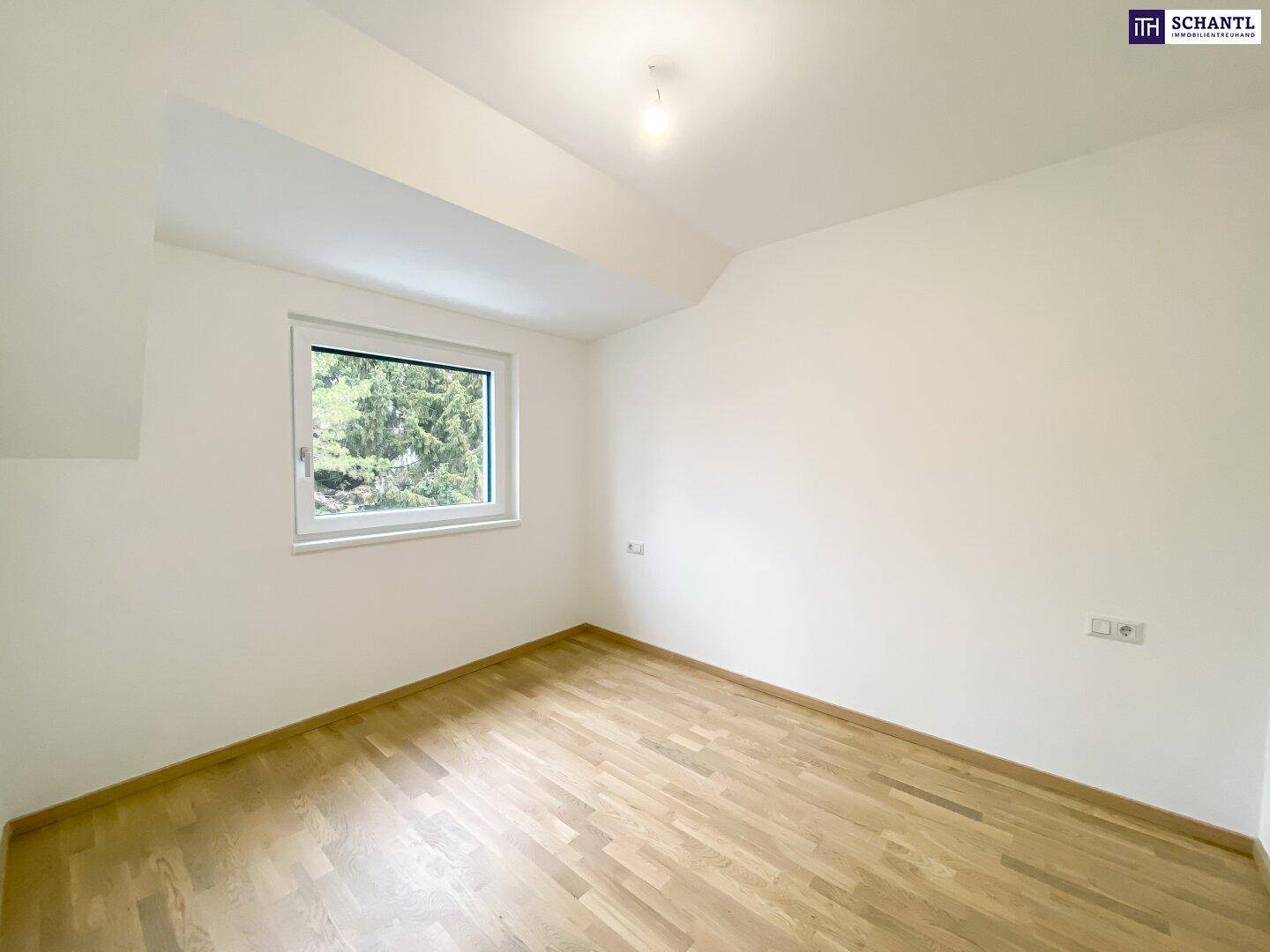Helles Schlafzimmer mit Parkettboden und einem Fenster mit Blick ins Grüne.