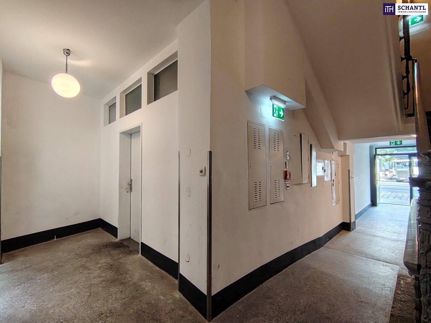 Heller Flur mit Aufzug, Treppenhaus und Ausgang zur Straße, ausgestattet mit Betonboden und weißen Wänden.
