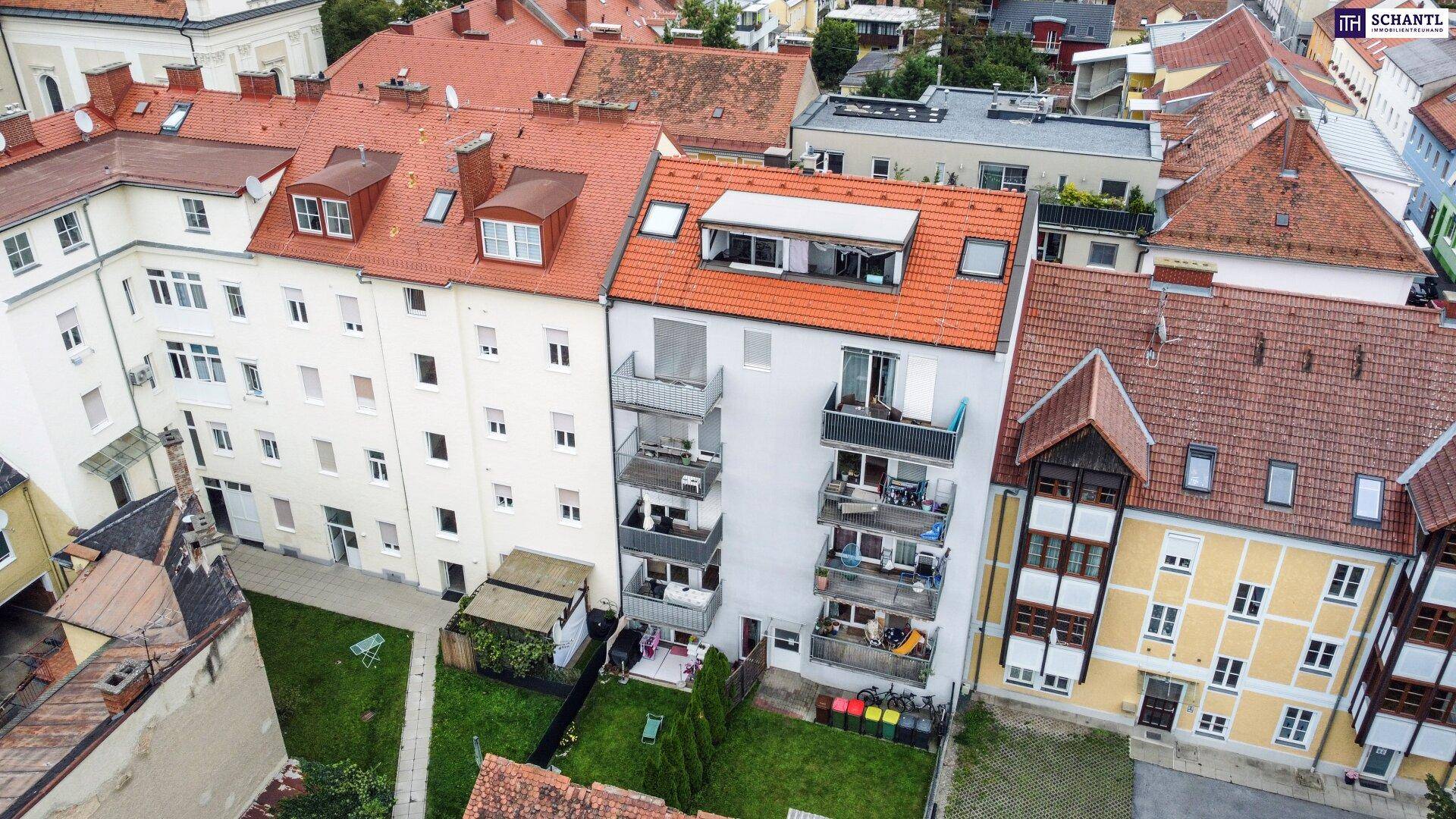 Rückansicht eines Wohnhauses mit mehreren Balkonen und einem kleinen begrünten Gartenbereich.