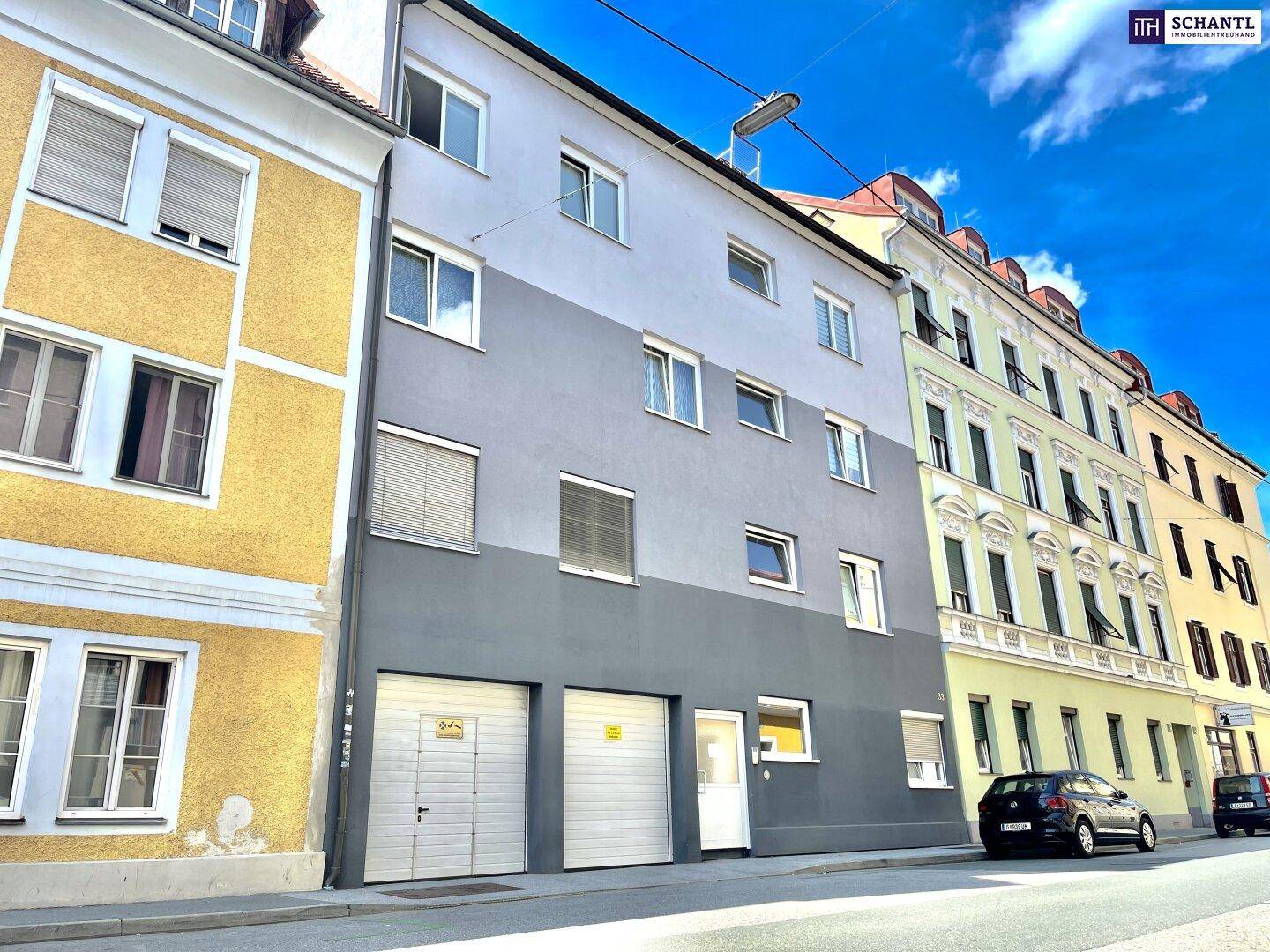 Straßenansicht eines modernisierten Wohnhauses mit zweifarbiger Fassade und Garagentoren.