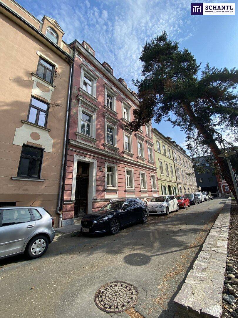 Historisches Gebäude mit rosafarbener Fassade und parkenden Autos an einer sonnigen Straße.