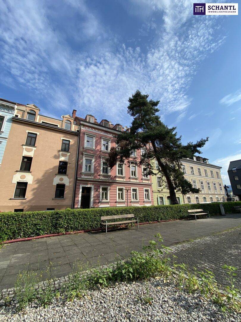 Reihe von historischen Gebäuden mit rosafarbener Fassade und einem Parkstreifen davor unter blauem Himmel.