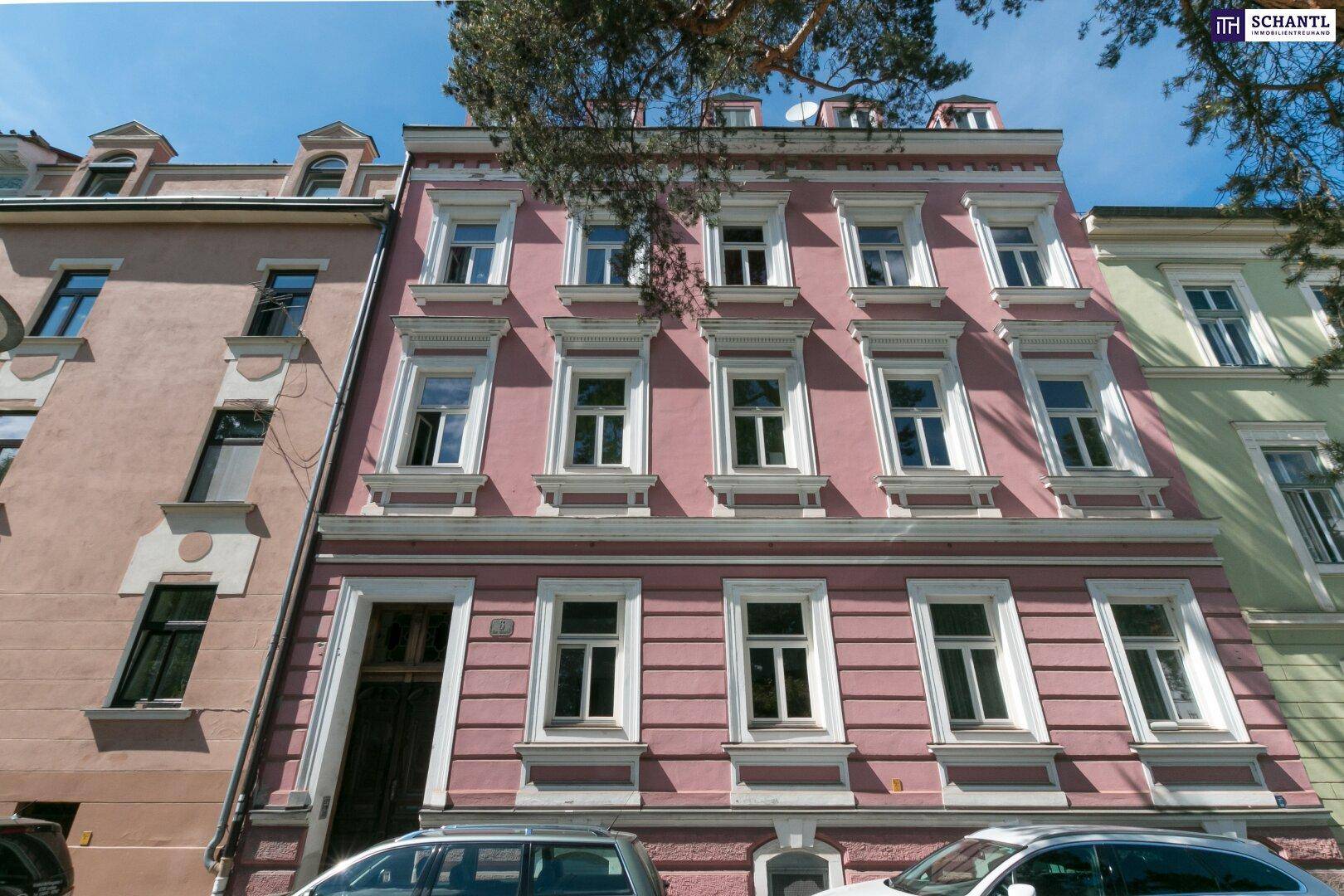 Frontansicht eines historischen Gebäudes mit rosafarbener Fassade und vielen Fenstern unter blauem Himmel.