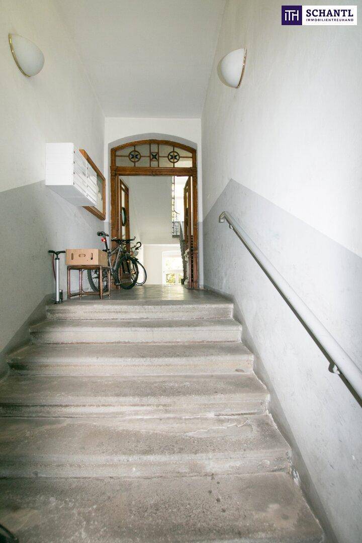 Eingangsbereich mit Steintreppe, Handlauf und einer verzierten Holztür, die in den Flur führt.