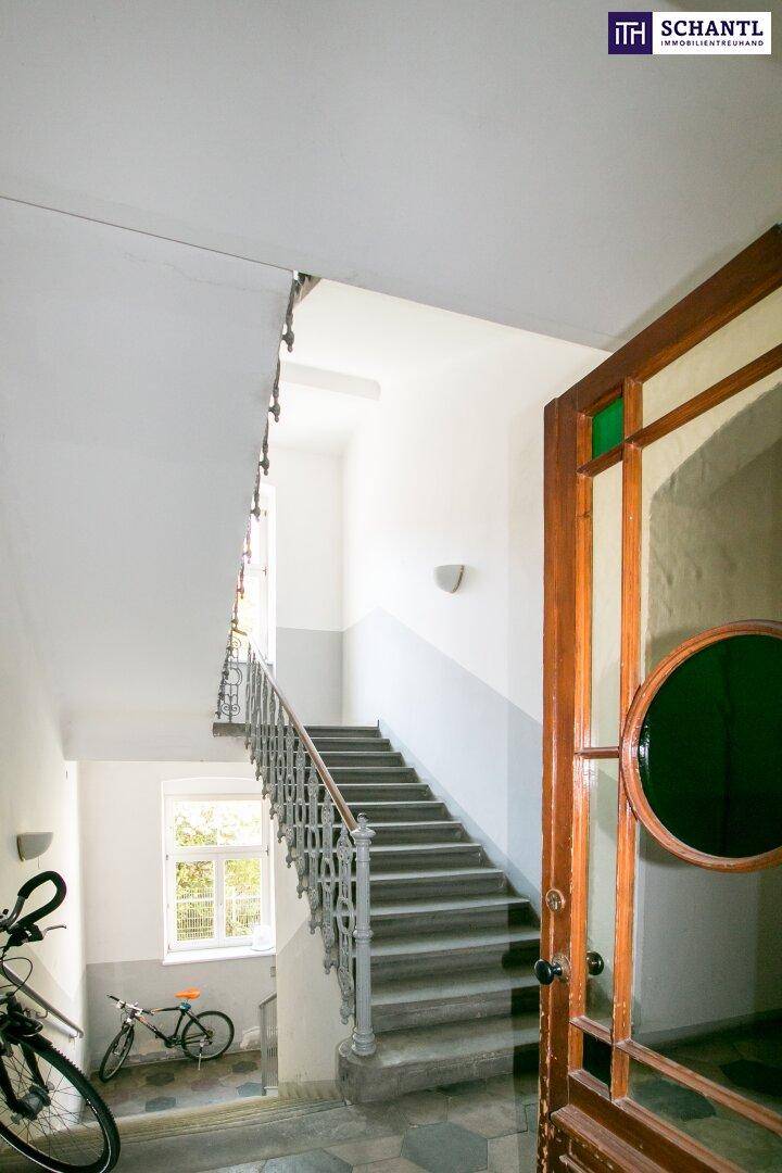 Historisches Treppenhaus mit schmiedeeisernem Geländer, Steinstufen und natürlichem Lichteinfall durch ein Fenster.