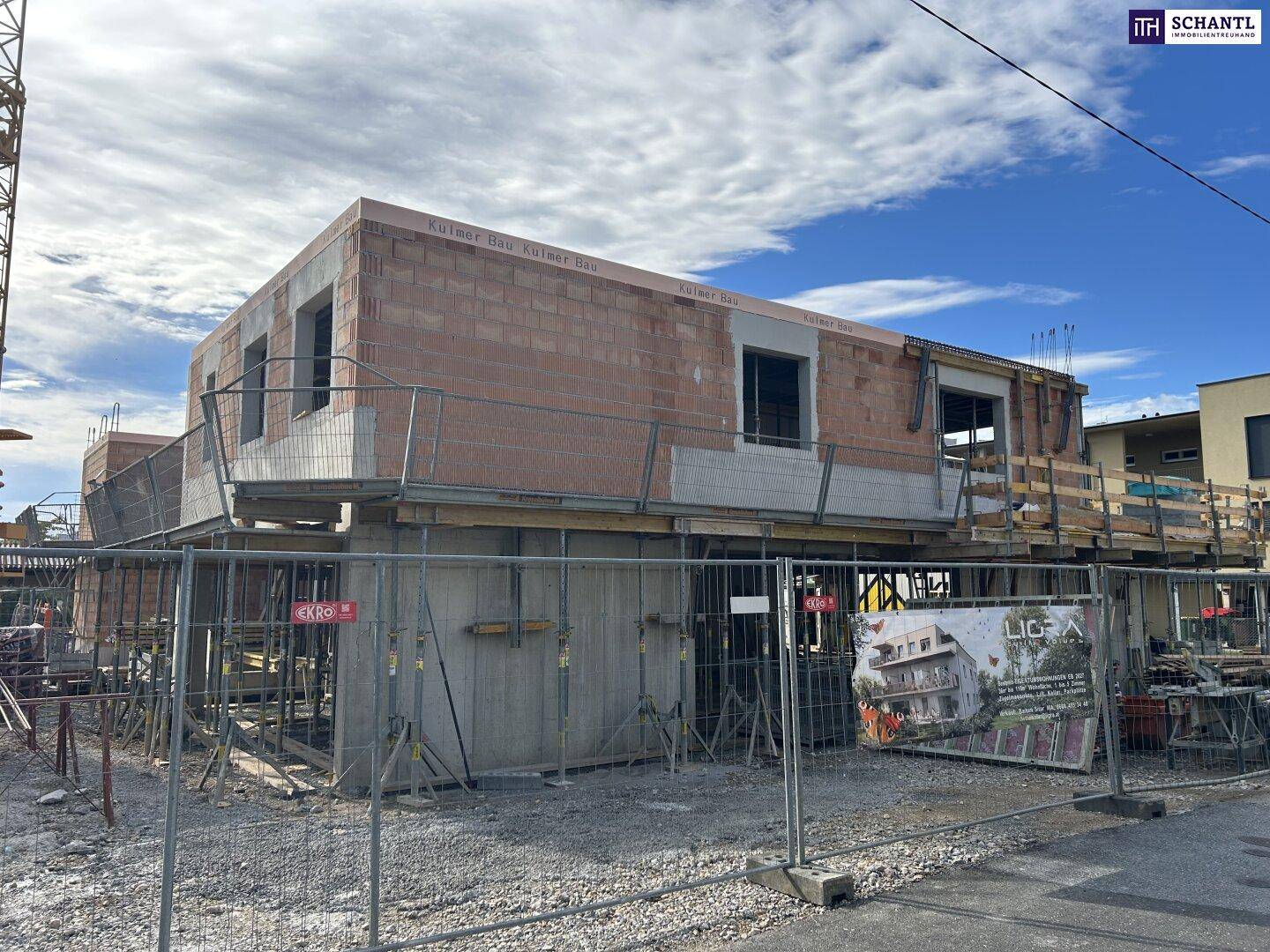 Baustelle eines Neubaus mit Ziegelwänden, Gerüsten, einem Baukran und Werbebannern für das Bauprojekt.