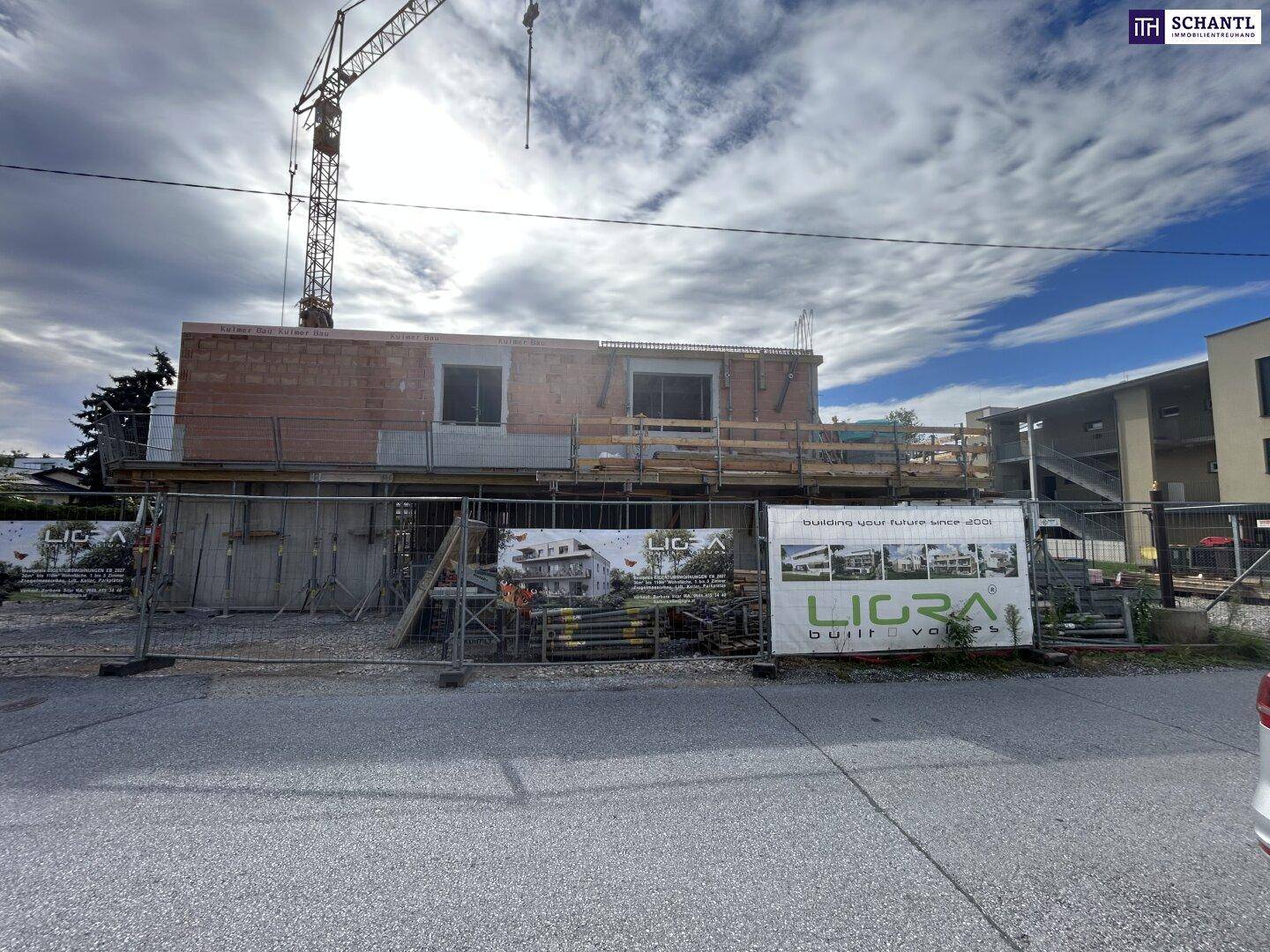Weitwinkelansicht der Baustelle mit dem im Rohbau befindlichen Gebäude und mehreren Werbebannern.