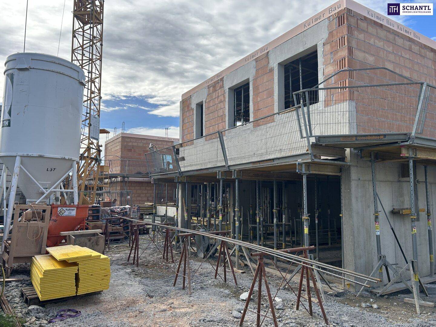 Baustelle mit einem im Rohbau befindlichen Gebäude, Baukran und Baumaterialien unter bewölktem Himmel.