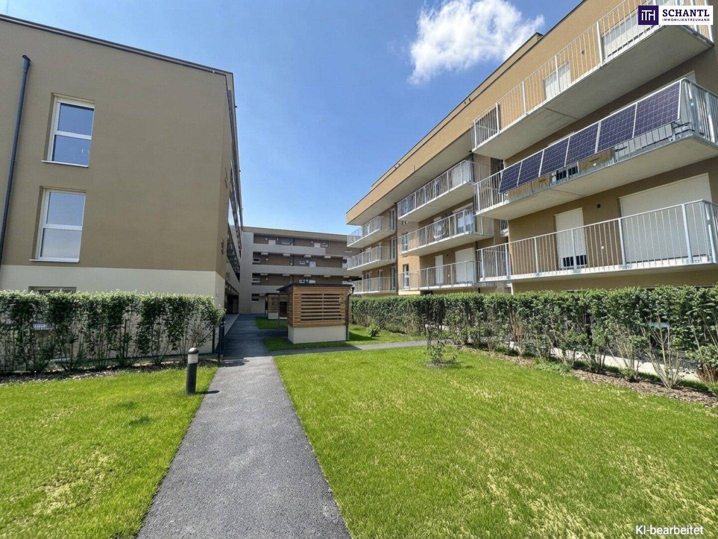 Außenansicht eines modernen Wohnkomplexes mit Balkonen, Solarpaneelen und einer gepflegten Rasenfläche.