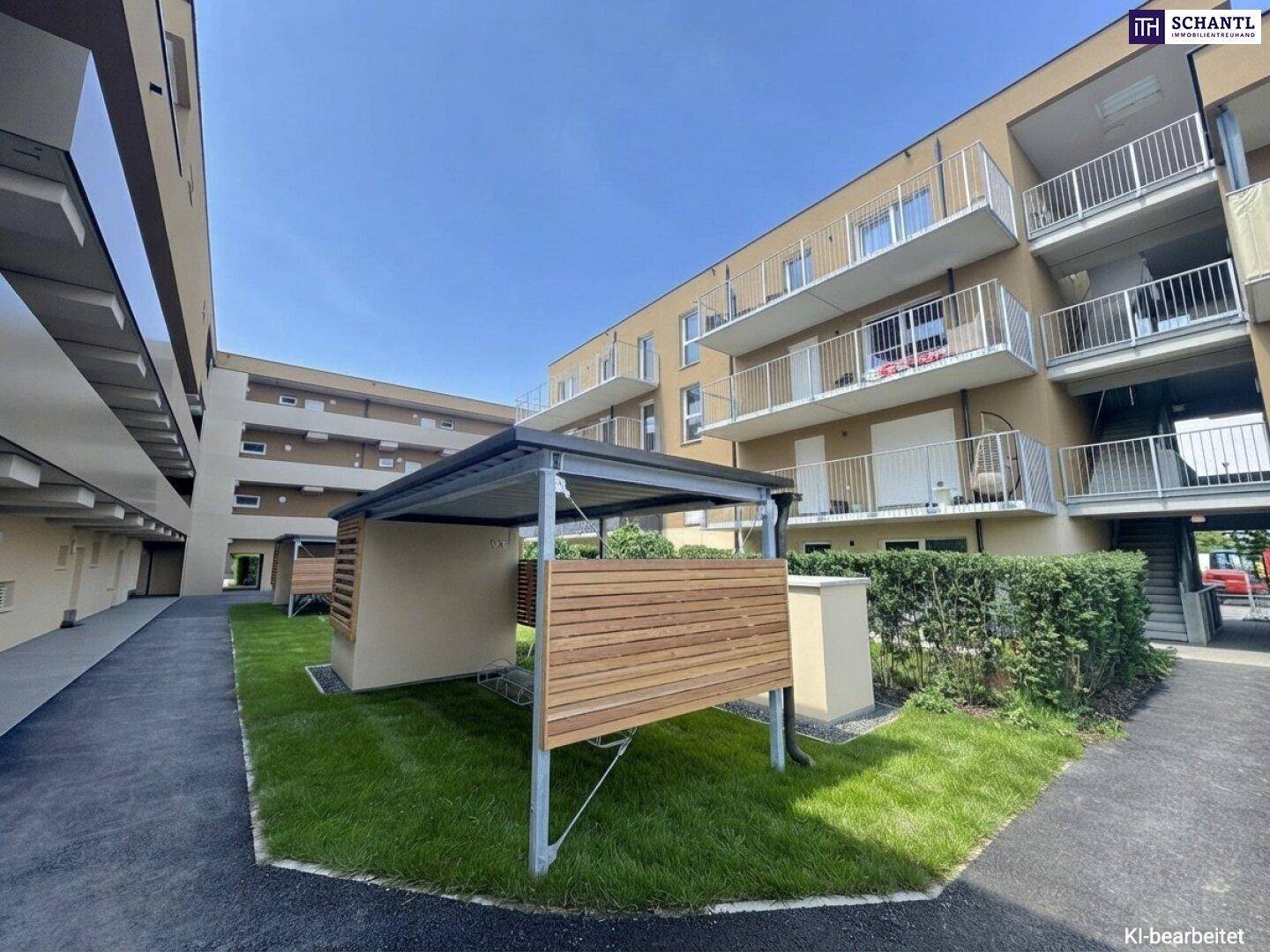 Außenbereich eines Wohnkomplexes mit Carport-Strukturen, Rasenflächen und modernen Gebäuden unter blauem Himmel.