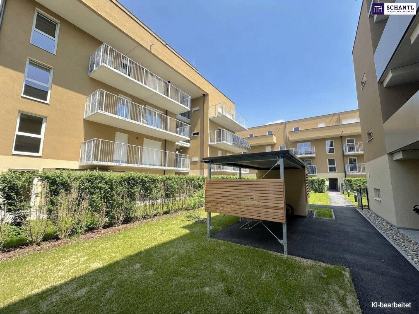 Wohngebäude mit Balkonen, Carport und einem gepflegten Rasenbereich unter blauem Himmel.