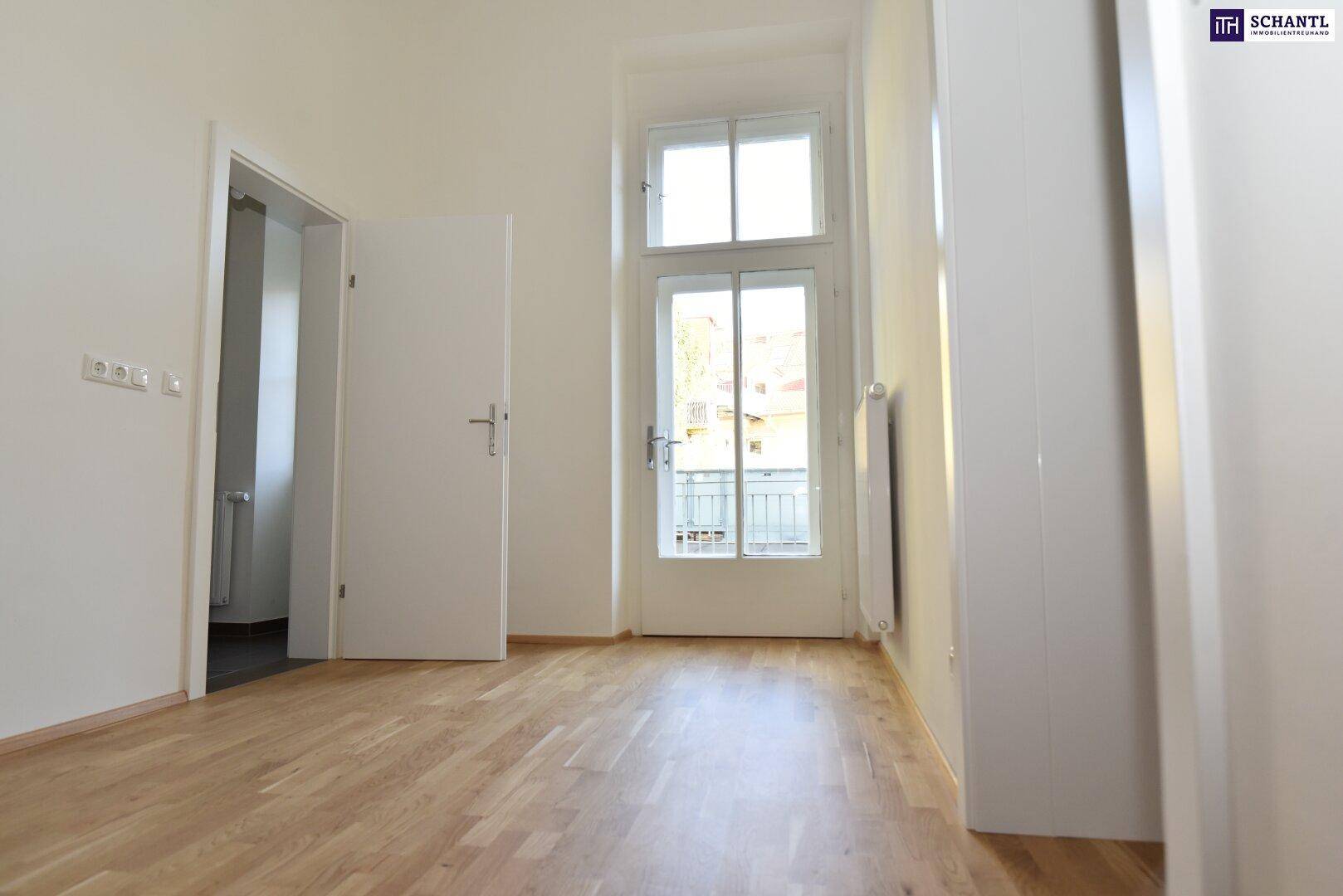 Heller Raum mit Holzboden und einer hohen Fenstertür, die zu einem kleinen Balkon führt.