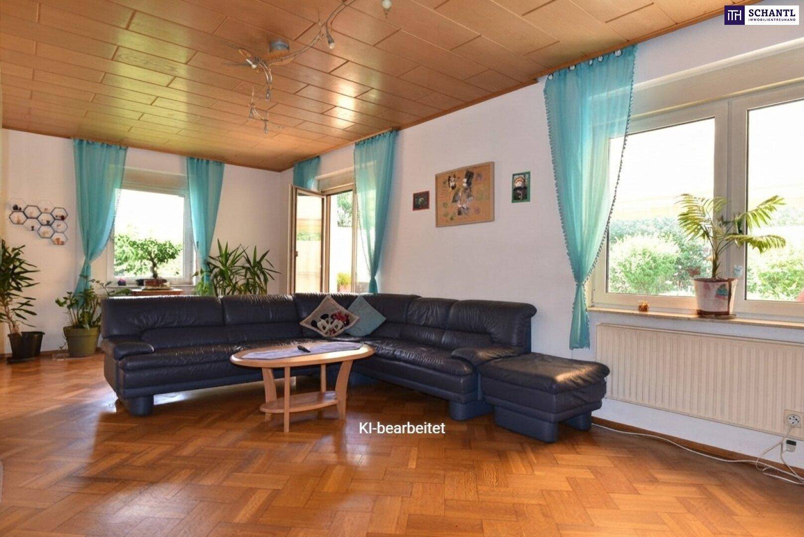 Gemütliches Wohnzimmer mit dunklem Ledersofa, Parkettboden und Holzdecke, hell durch große Fenster.