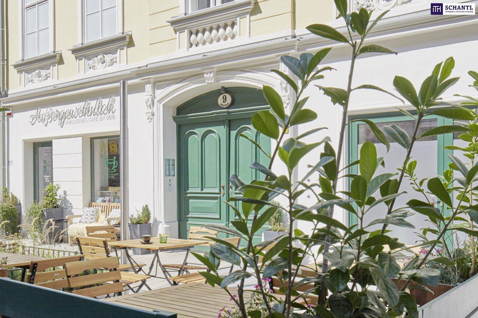 Eingangsbereich eines Gebäudes mit grüner Doppeltür und Außensitzbereich eines Cafés.
