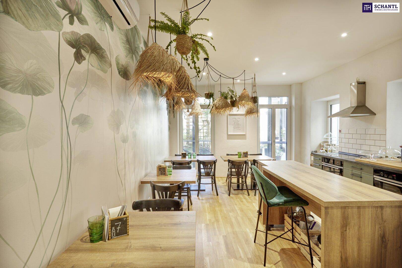 Langer Raum eines Cafés mit Holztischen, Bar und dekorativer Pflanzenwand.