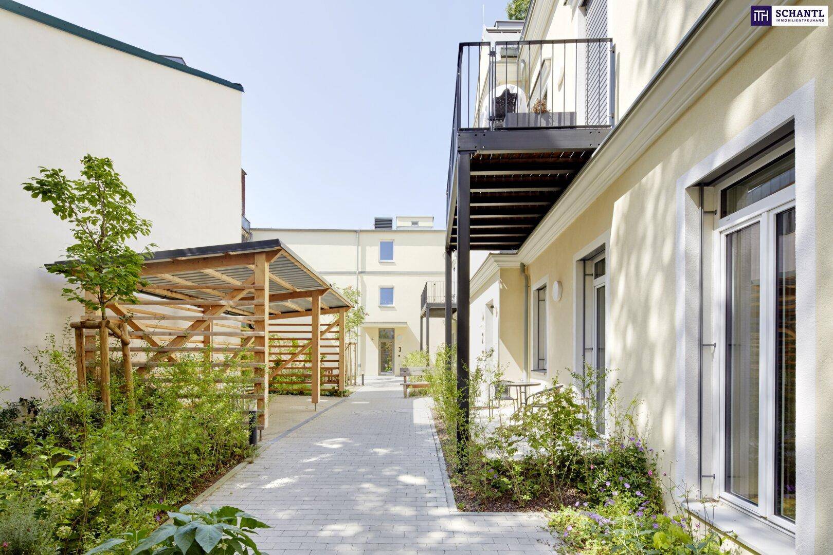 Innenhof mit gepflastertem Weg, Grünflächen und Balkonen an der Gebäudefassade.