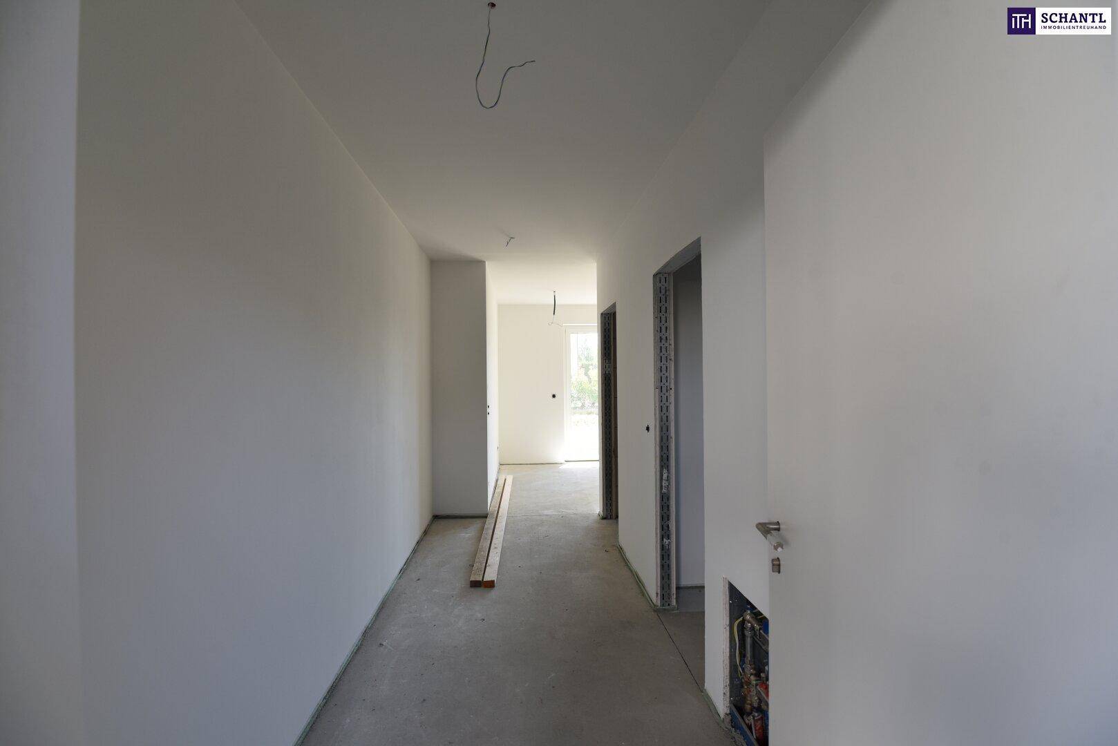 Langer, heller Flur im Rohbau mit weiß gestrichenen Wänden und Betonboden.