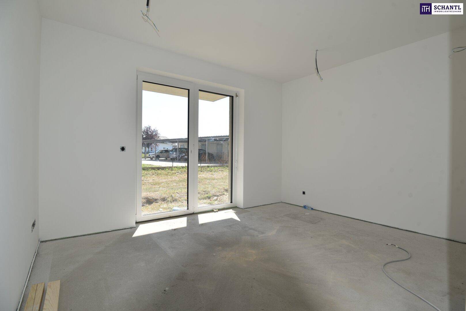 Heller Wohnraum im Rohbau mit großer Terrassentür und Blick ins Grüne.