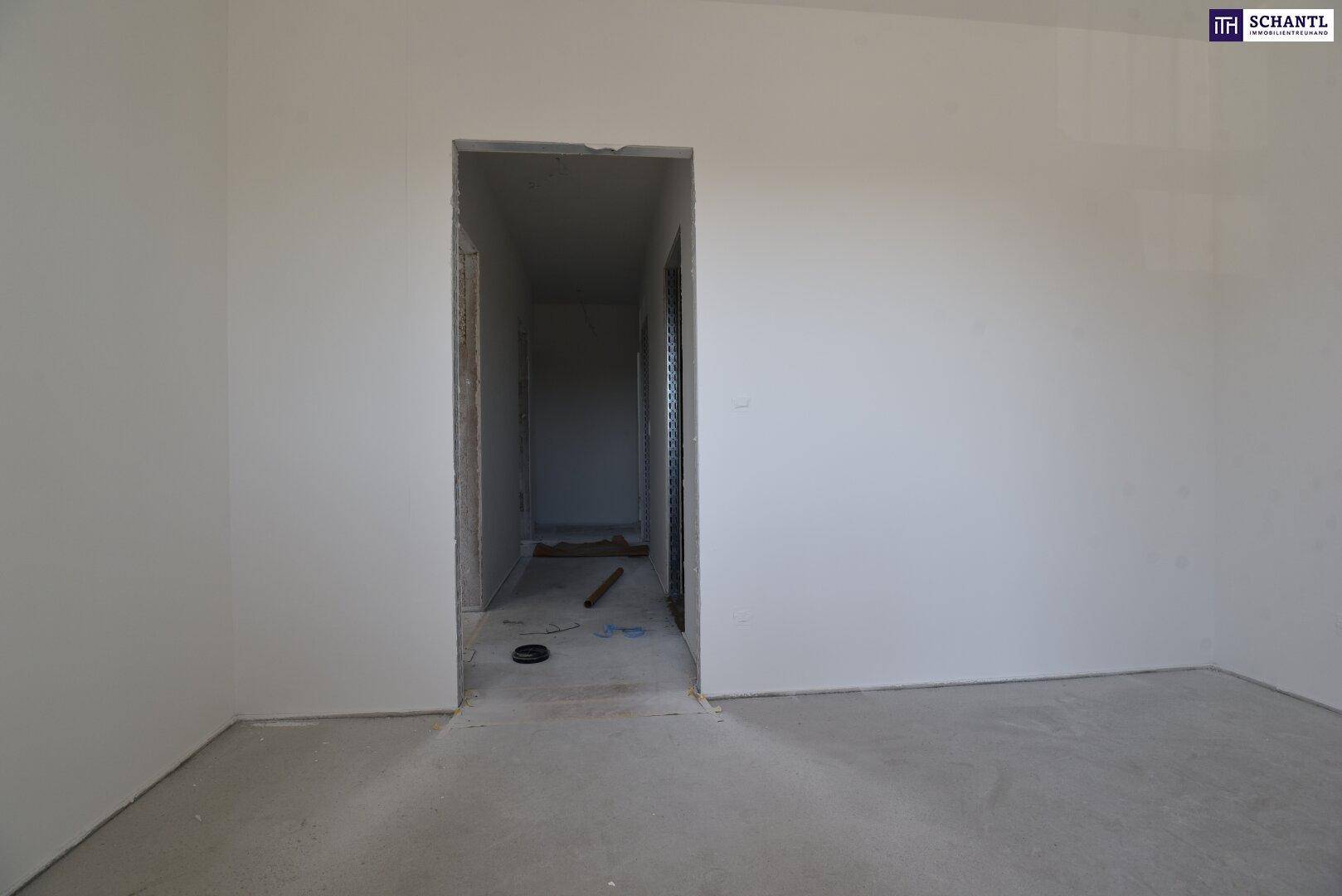 Unmöblierter Raum im Rohbau mit Türöffnung zu einem weiteren Flur.