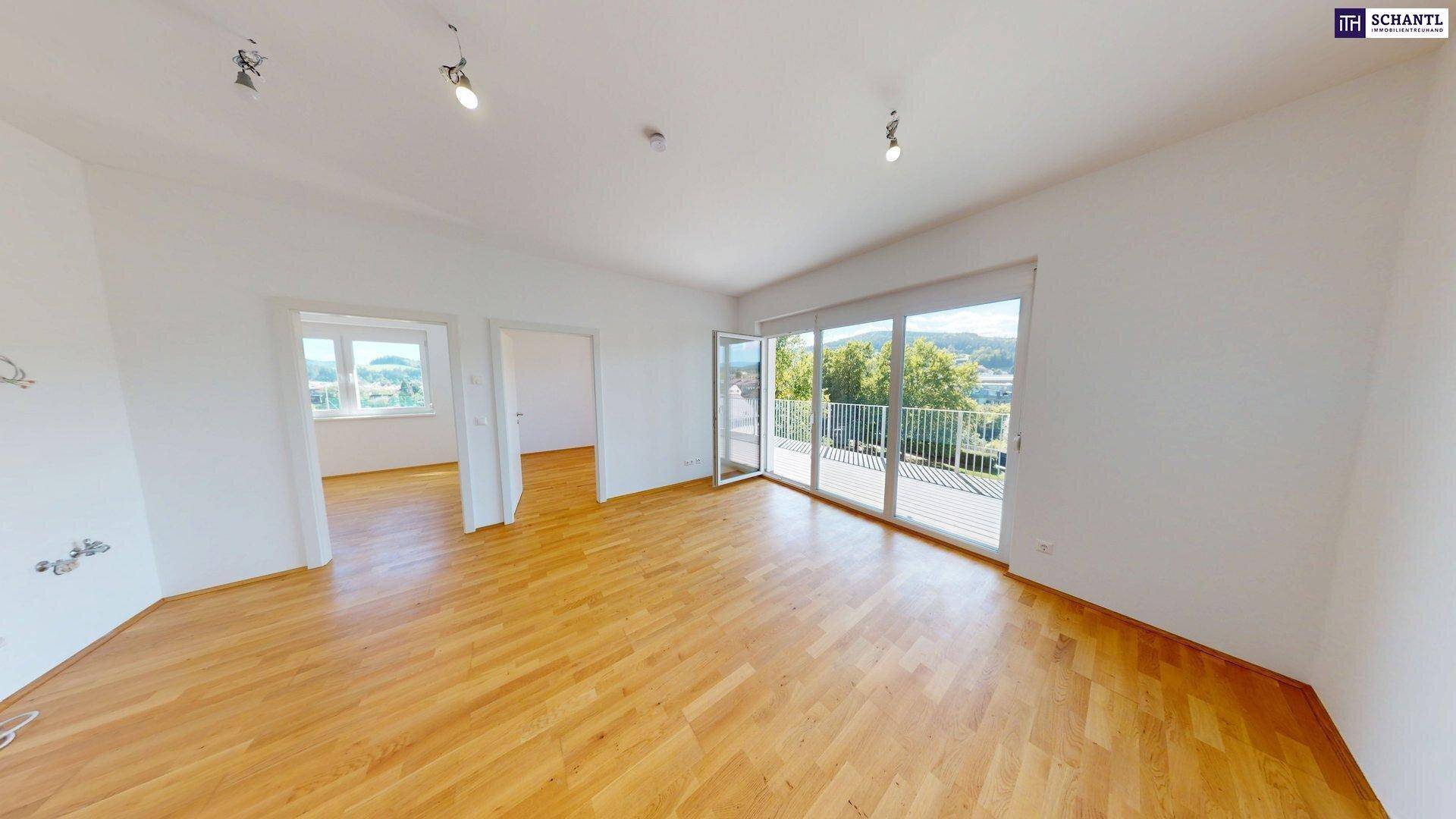 Heller, leerer Wohnraum mit Holzboden und Zugang zu einem Balkon mit Weitblick.