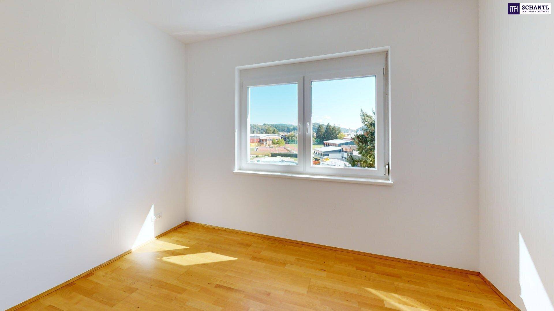 Heller Raum mit Holzboden und großem Fenster, das einen Blick auf die Umgebung bietet.