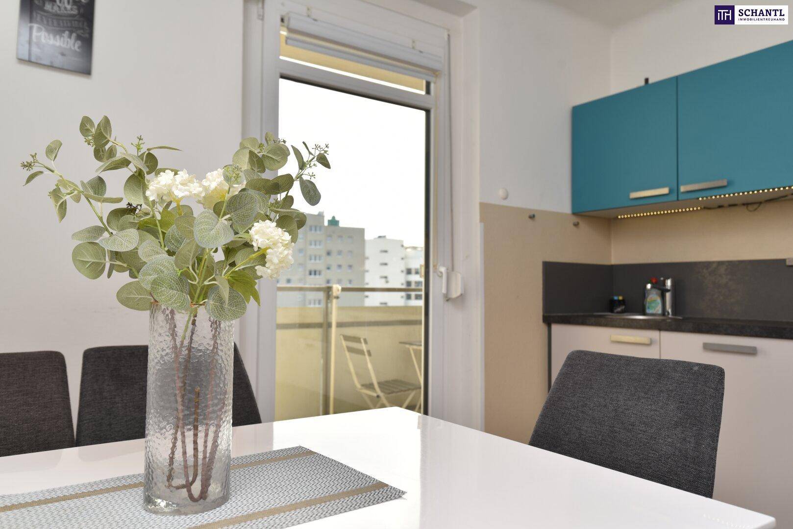 Essbereich mit Blumenvase und Blick auf die moderne Küche sowie den angrenzenden Balkon.