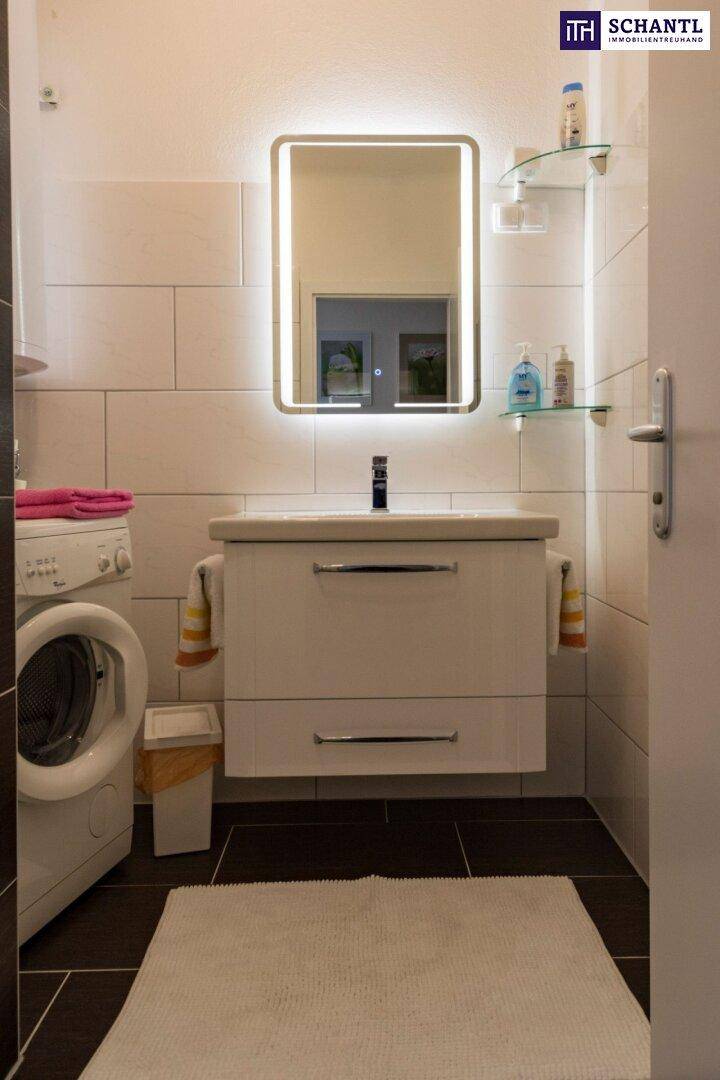 Modernes Badezimmer mit beleuchtetem Spiegel, Waschtisch und Waschmaschine.