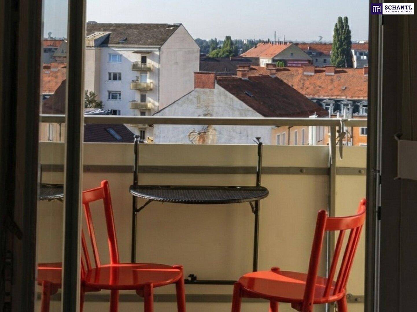Gemütlicher Balkon mit roten Stühlen und einem kleinen Tisch, der einen weiten Blick über die städtischen Dächer bietet.