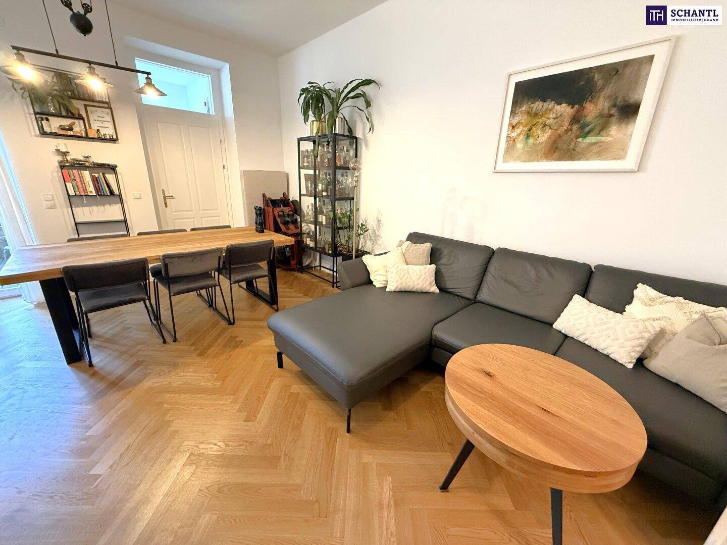 Geräumiger Wohn- und Essbereich mit bequemer Couch, großem Esstisch und elegantem Fischgrätparkett.