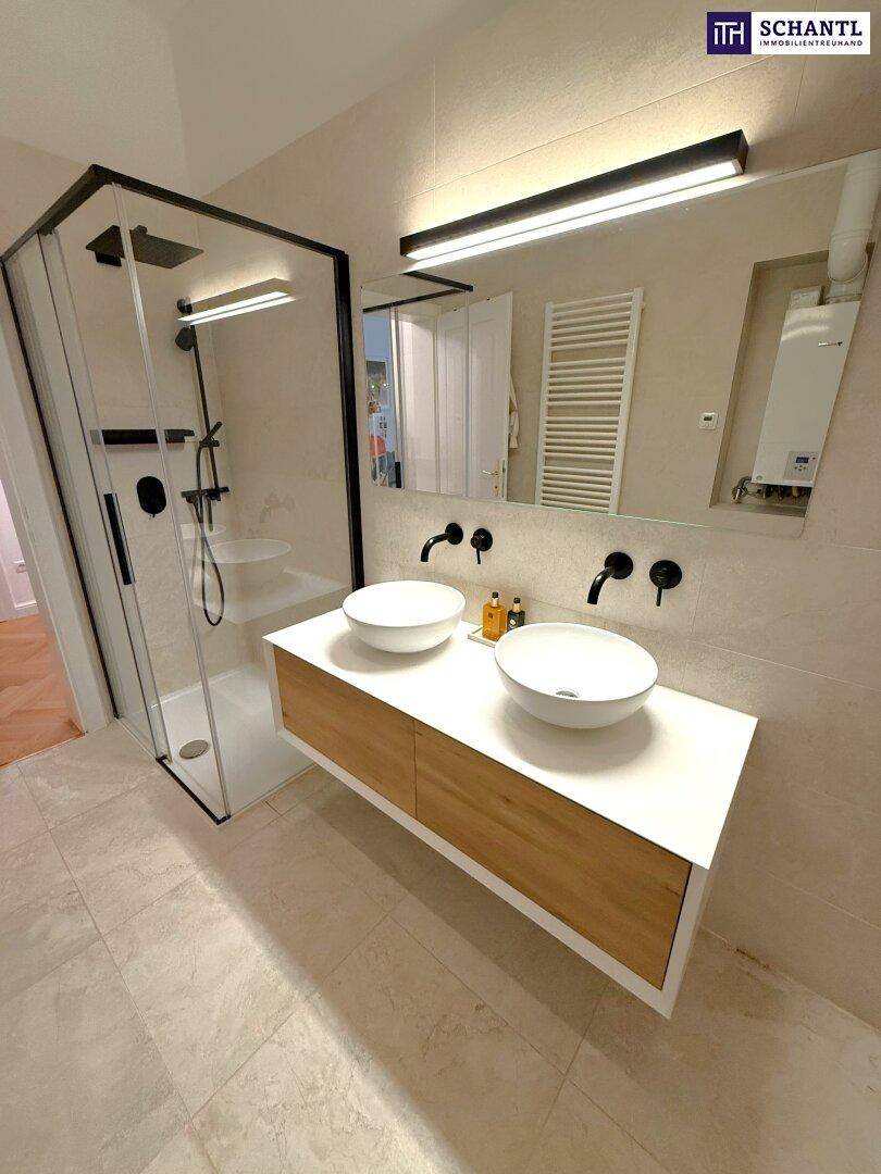 Modernes Badezimmer mit Doppelwaschbecken, begehbarer Dusche und hellen Fliesen.