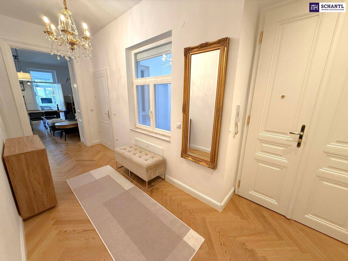 Eleganter Flur mit Fischgrätparkett, Kronleuchter und großem vergoldeten Spiegel.