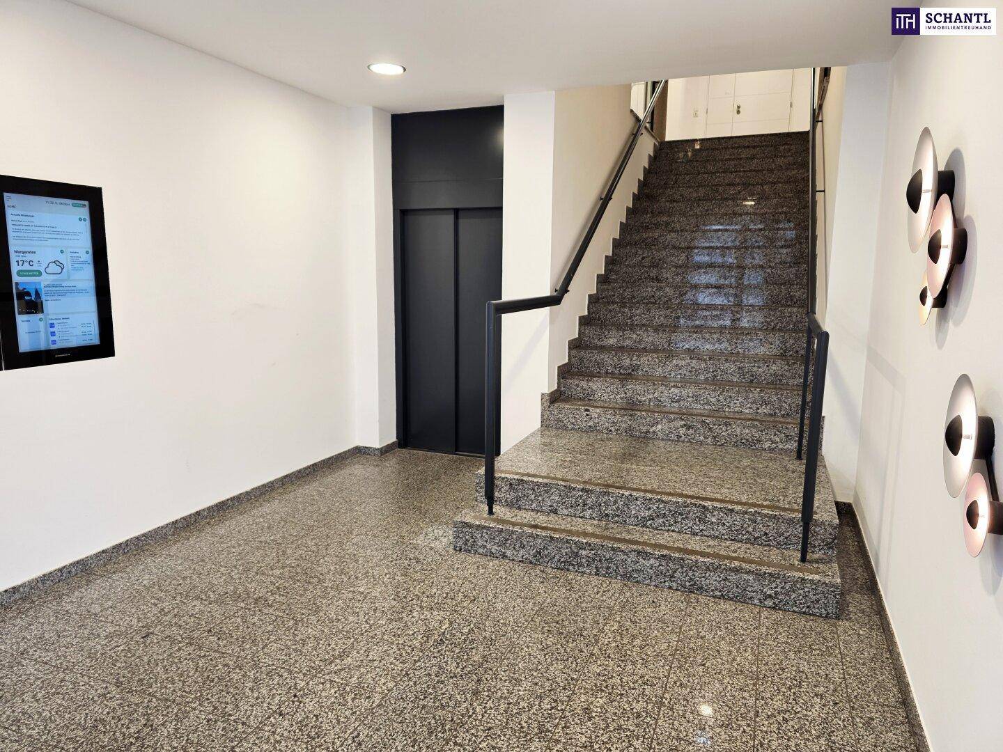 Heller Eingangsbereich mit Granitboden, Treppenhaus und modernem Aufzug.