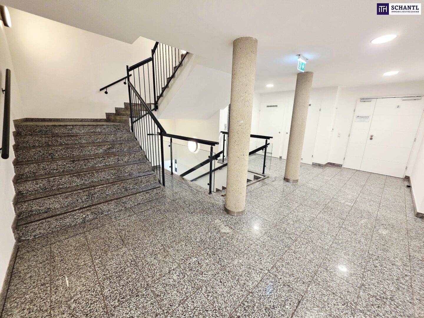Geräumiger Treppenaufgang mit Granitboden, Säulen und Metallgeländer im Gemeinschaftsbereich.