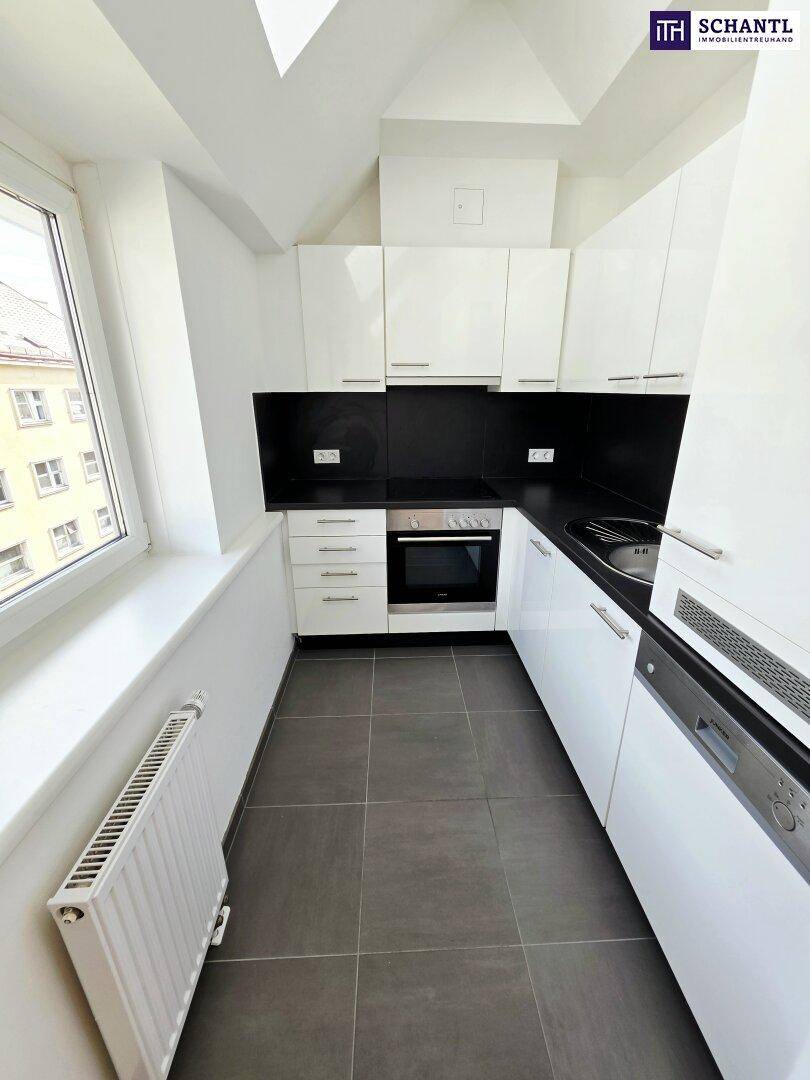 Moderne weiße Küche mit schwarzen Arbeitsplatten, Fliesenboden und Fenster in der Dachschräge.