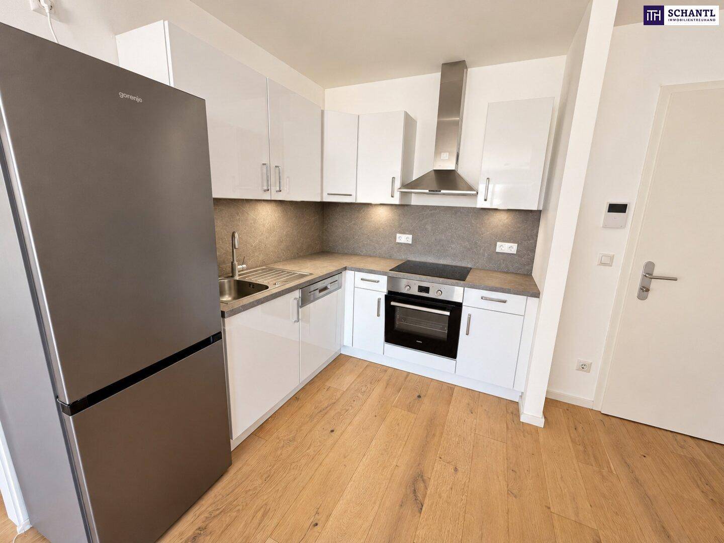 Moderne Einbauküche mit weißen Hochglanzfronten, integrierten Geräten und Holzboden.