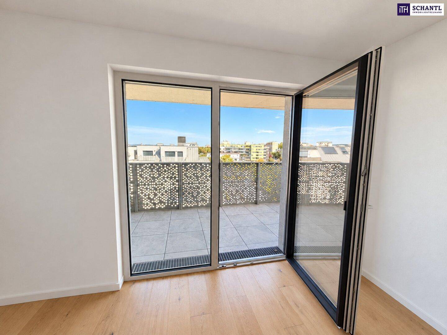 Helles Zimmer mit Holzboden und großem Fenster, das den Zugang zum Balkon ermöglicht.