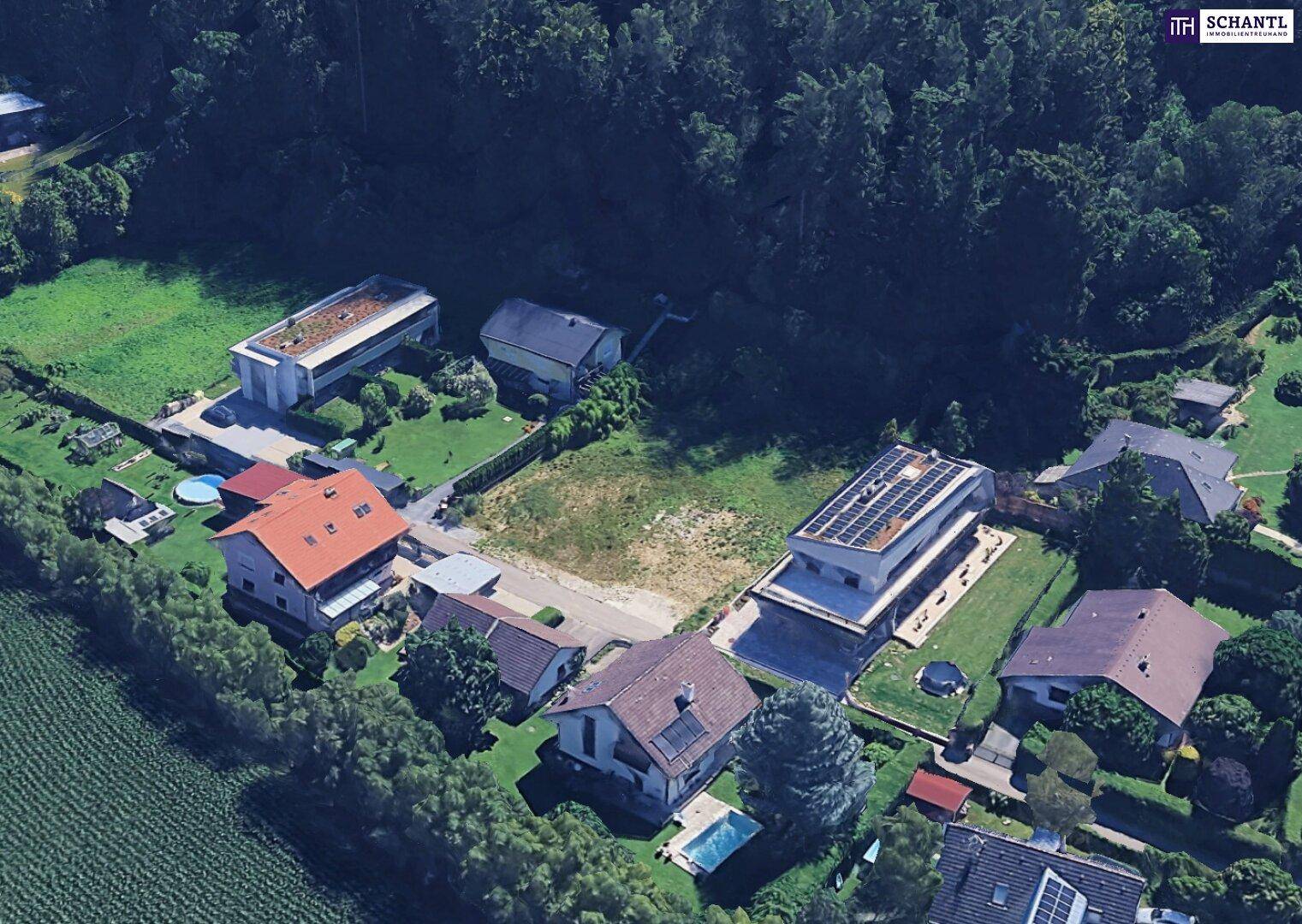 Luftaufnahme eines Wohngebiets mit Einfamilienhäusern, Gärten und einem freien Baugrundstück.