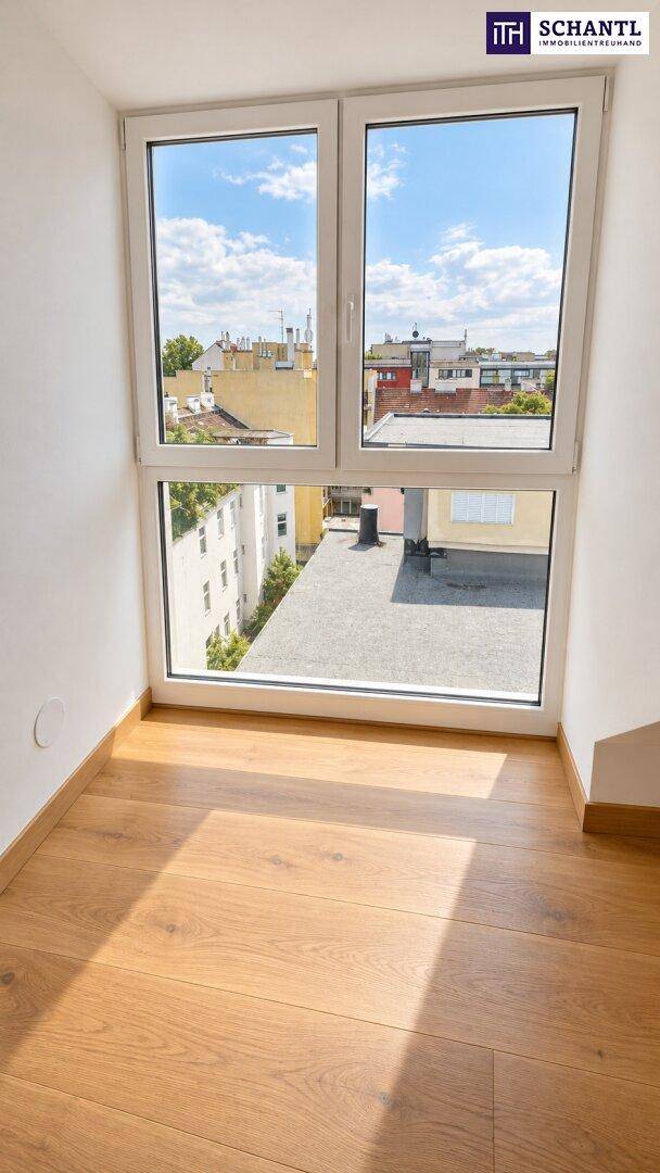 Kleiner Raum mit großem Fenster und Blick auf die umliegenden Dächer, mit Holzparkett.