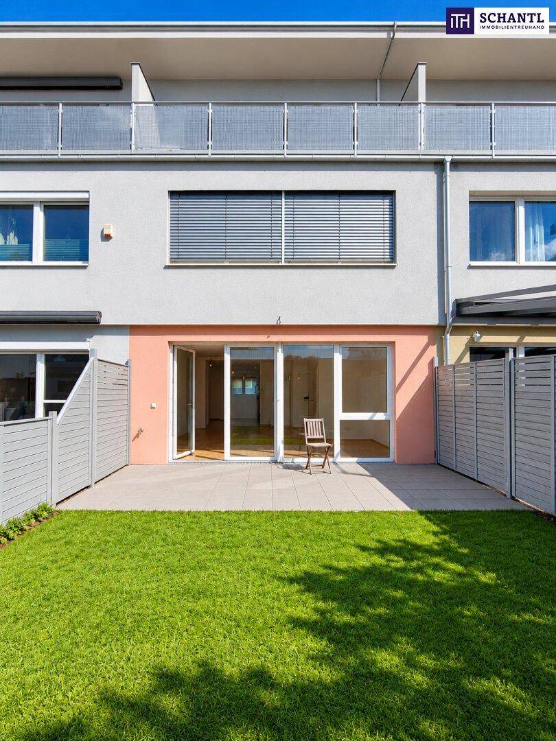Moderne Reihenhausfassade mit privatem Garten, Terrasse und großen Fenstern im Erdgeschoss.
