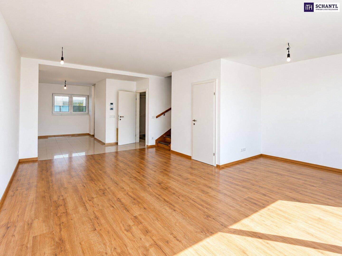 Geräumiges Wohnzimmer mit Laminatboden und offenem Übergang zu weiteren Räumen und Treppe.