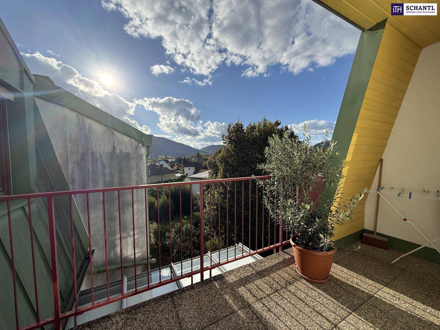 Sonniger Balkon mit Fliesenboden, rotem Geländer und weitem Blick auf die Berge und Umgebung.