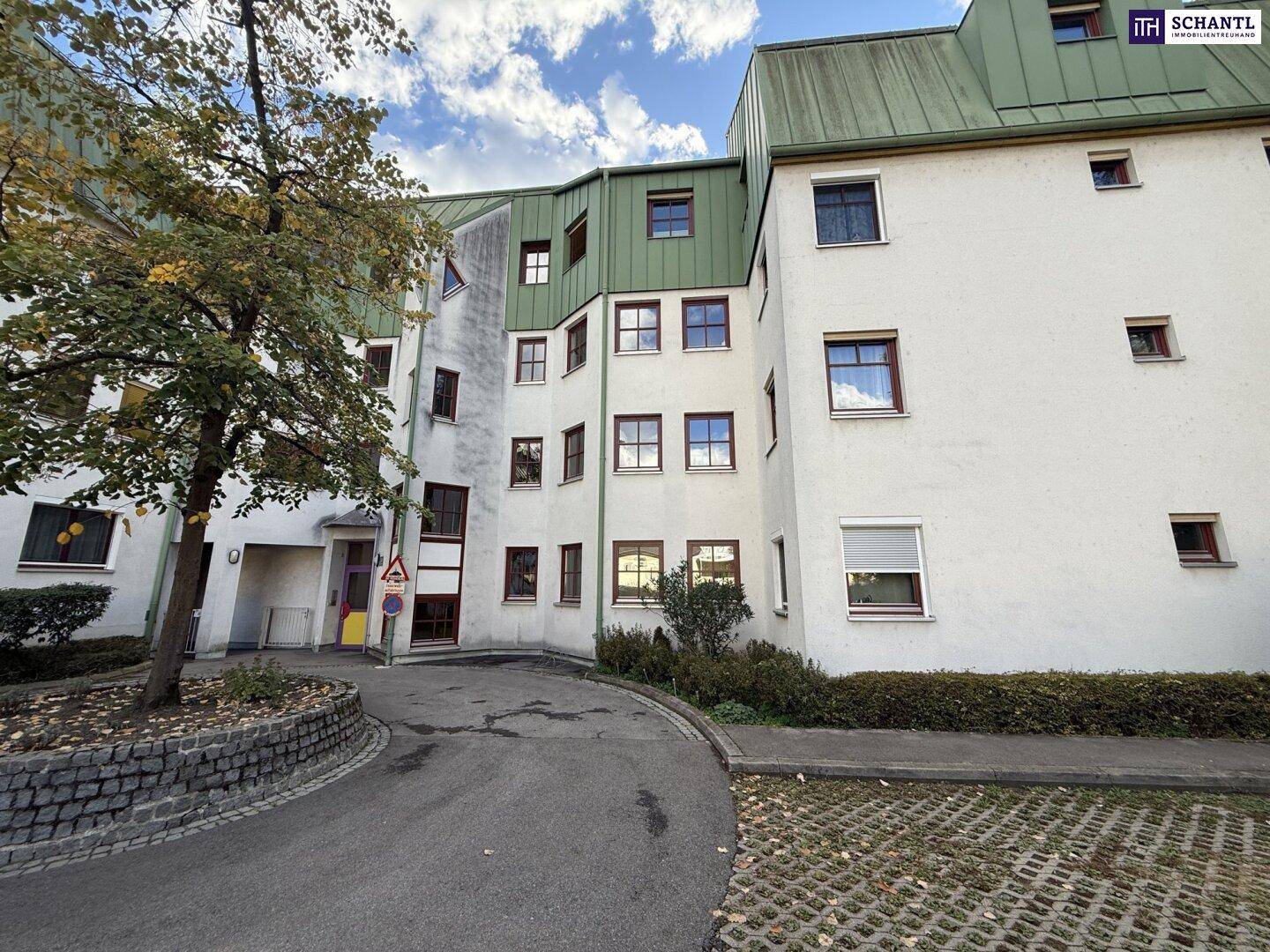 Außenansicht des Wohngebäudes mit weißer Fassade, grünem Dach und gepflastertem Vorplatz.