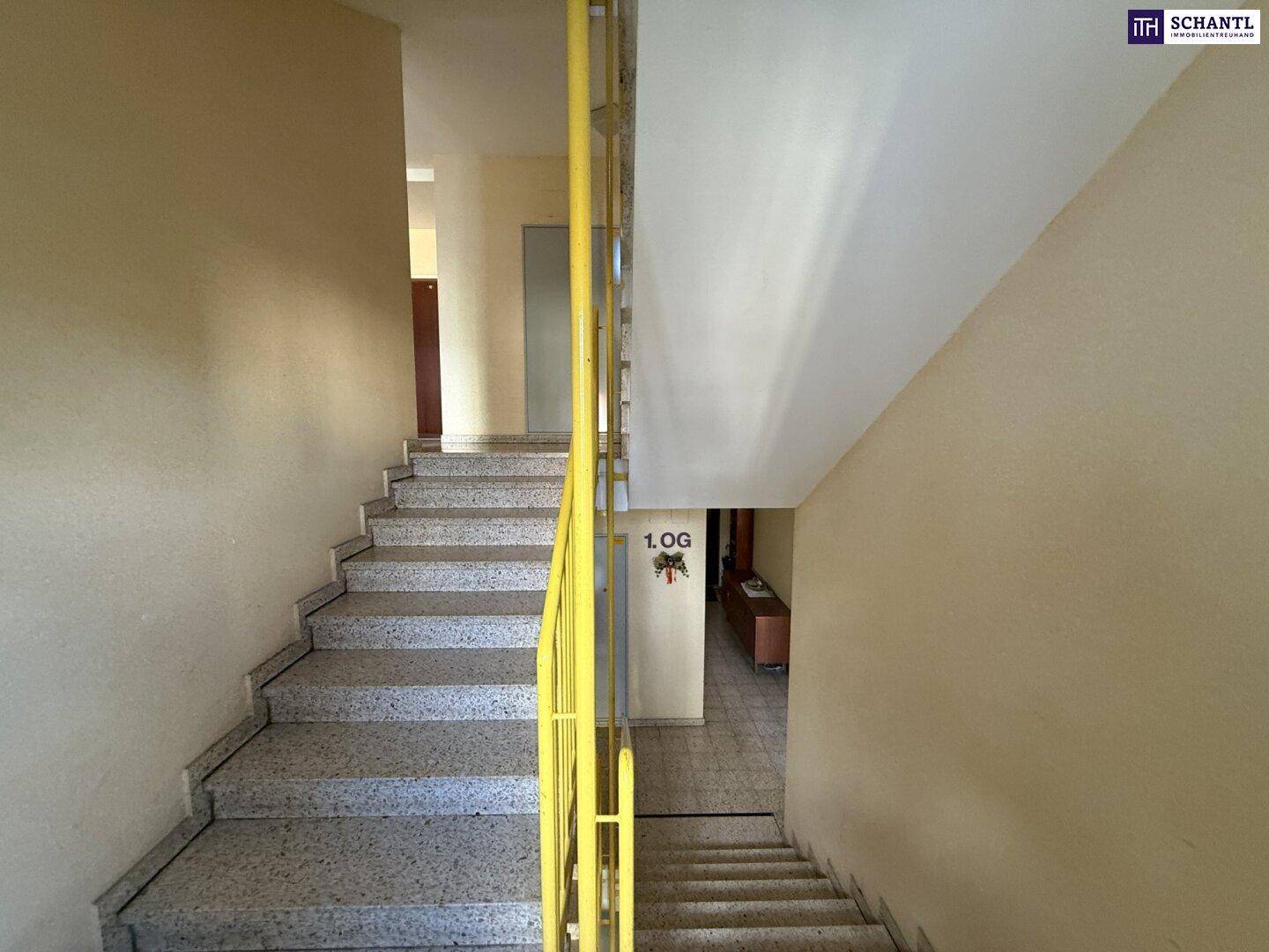 Treppenhaus mit Steinstufen und gelbem Geländer, führt zum ersten Obergeschoss.