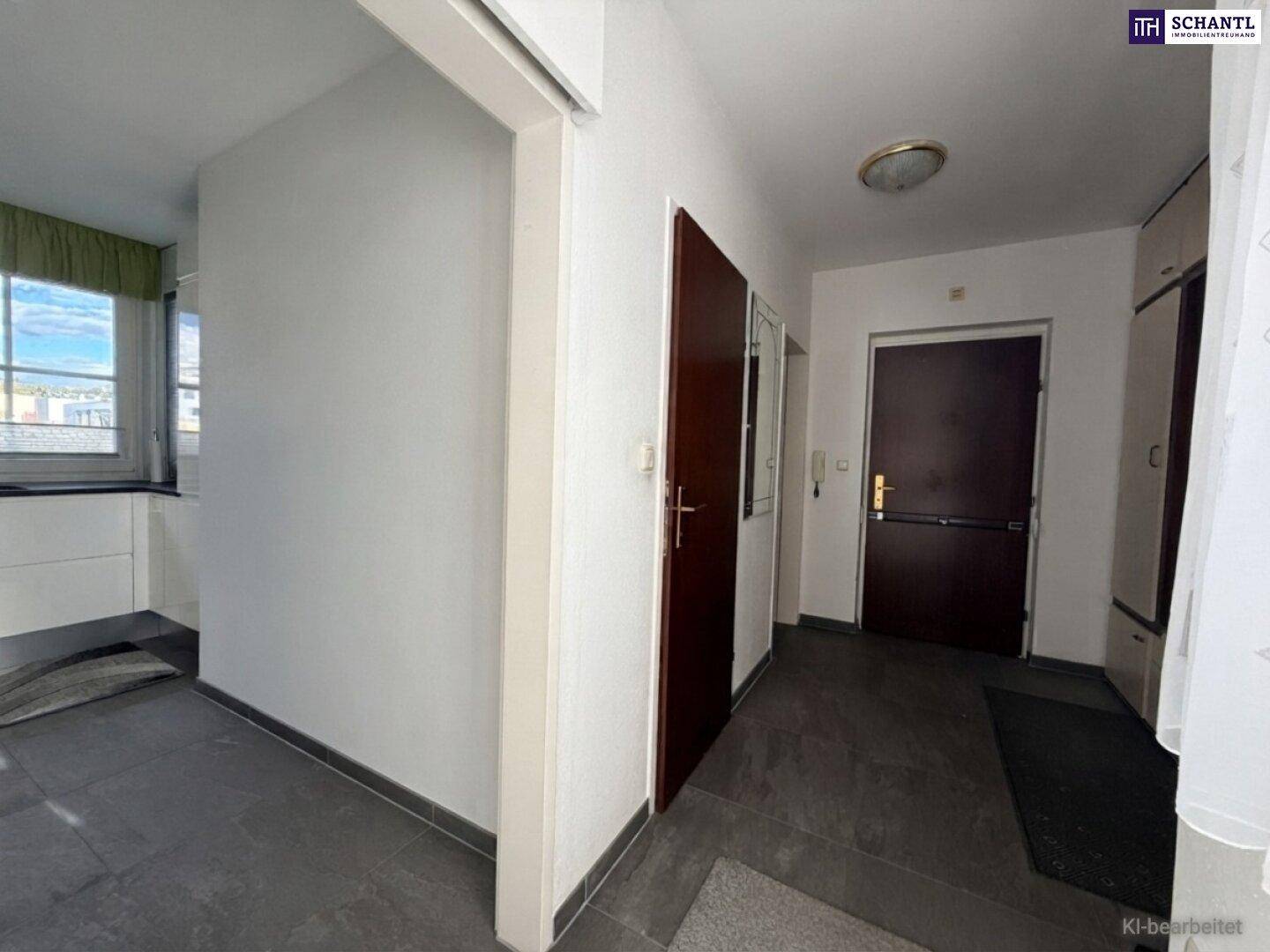 Heller Flur mit dunklem Fliesenboden und weißen Wänden, führt zu verschiedenen Räumen.