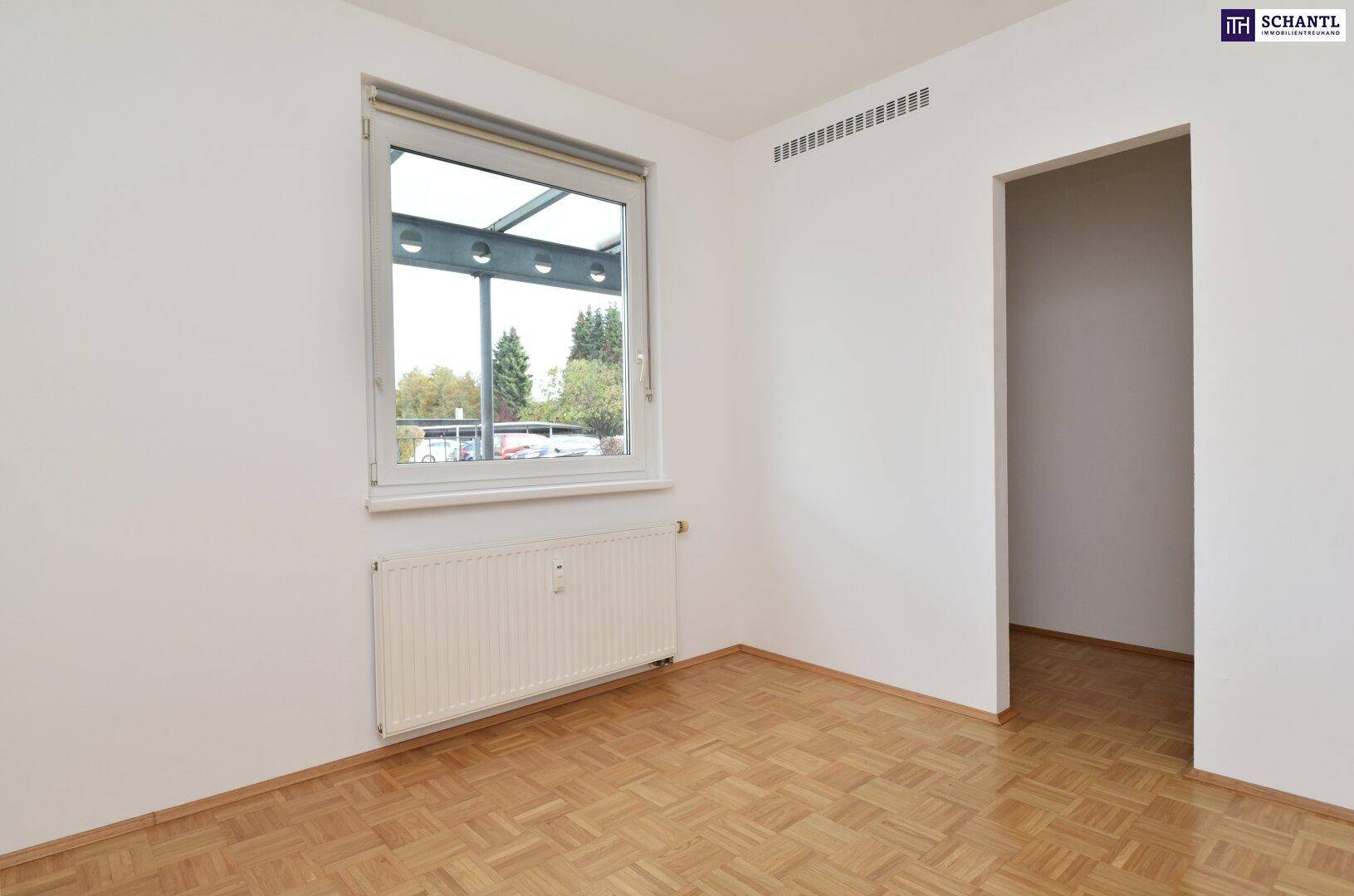 Helles Schlafzimmer mit Parkettboden und Fenster, das viel Tageslicht hereinlässt.