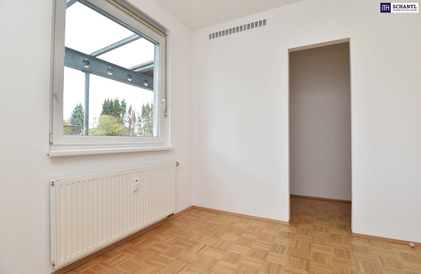 Helles Schlafzimmer mit Parkettboden und Fenster, das viel Tageslicht hereinlässt.