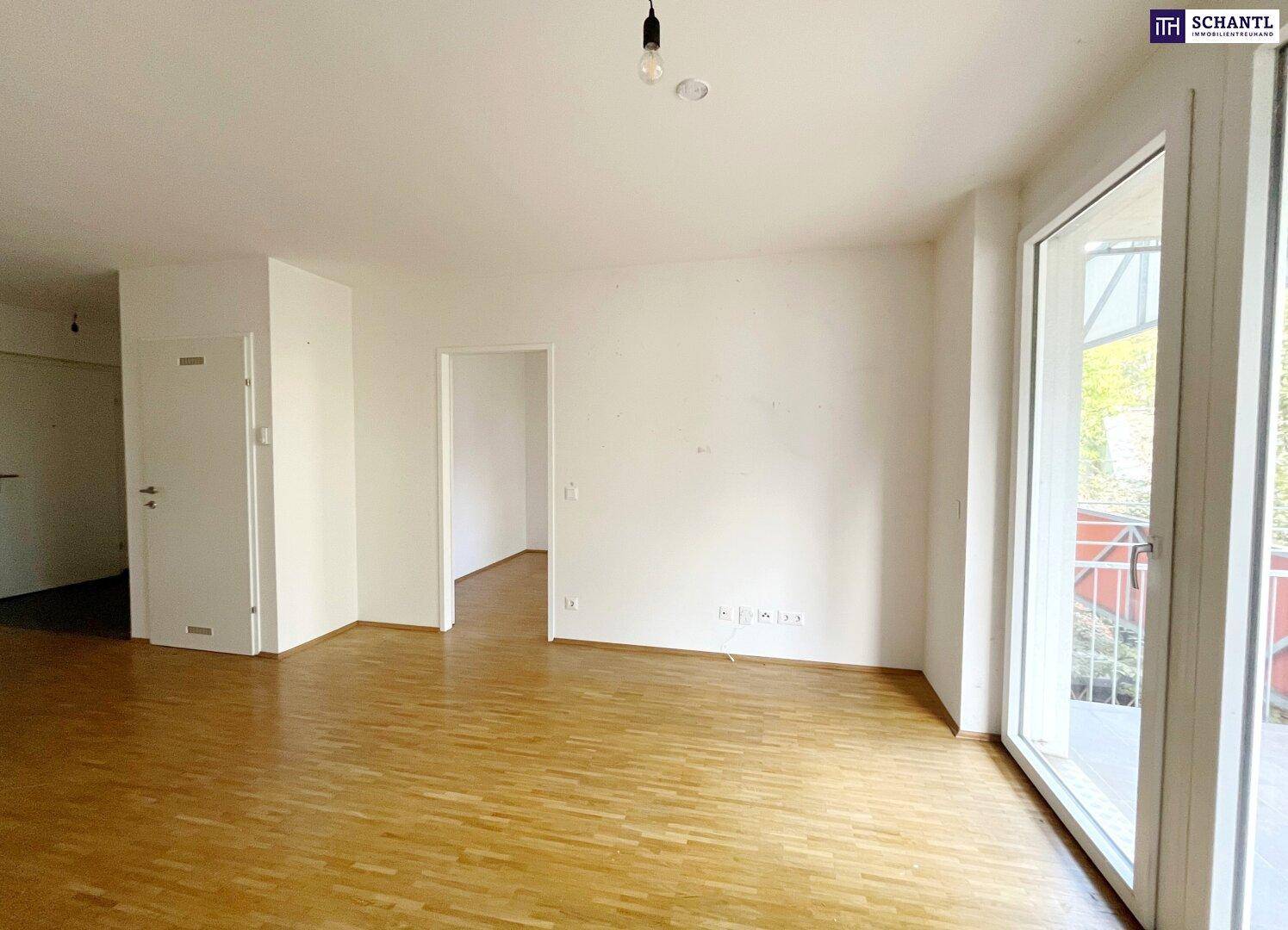 Heller Wohnbereich mit Parkettboden und großen Fenstern, die den Blick ins Grüne freigeben.